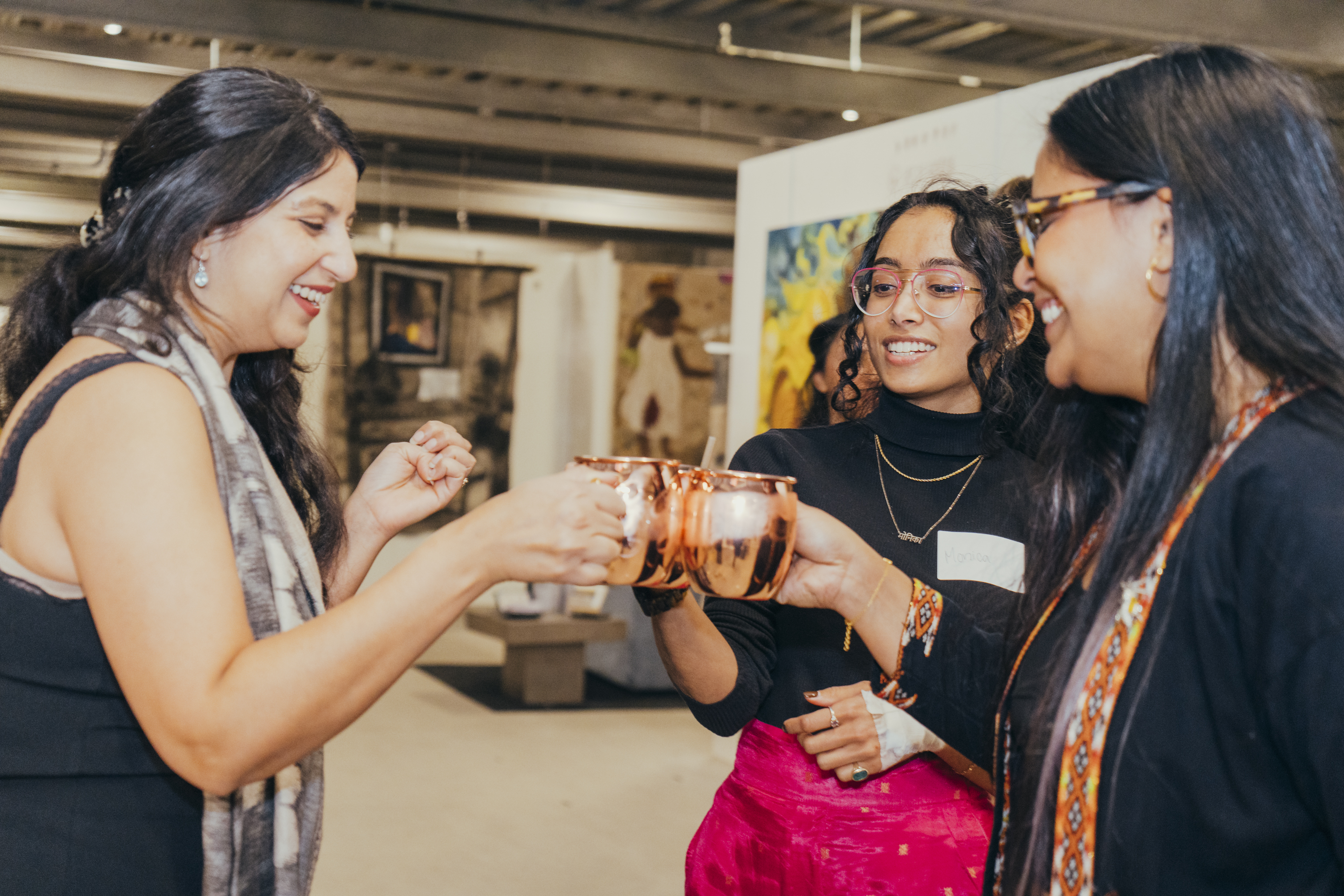 Brown Girls clinking copper mugs at Investing in Art — the room mid-toast